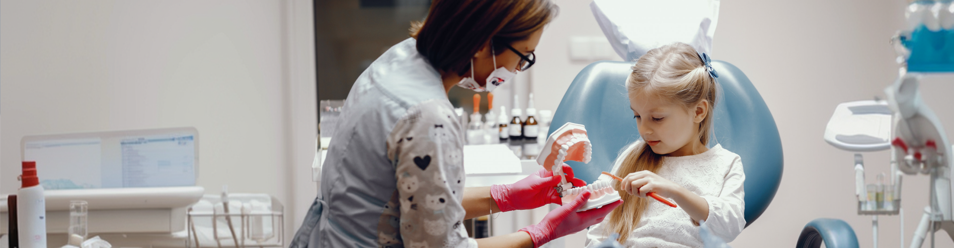 Pediatric dentist teaching a young girl proper brushing techniques with a dental model.